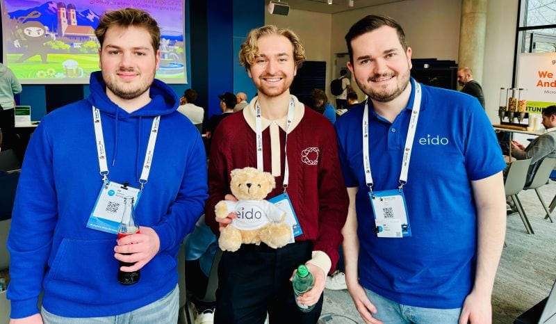 Three people at the event wearing conference lanyards, one holding a small Odie bear.